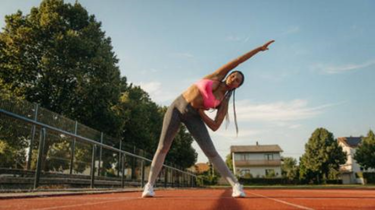 A person stretching on a track while performing an outdoor exercise.